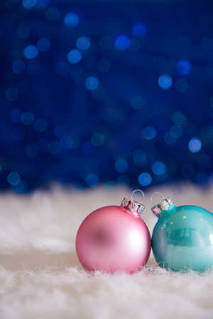 Two Christmas balls on white fur with garland lights on blue bokeh background. New year card with empty space. Xmas festive decoration.の写真素材