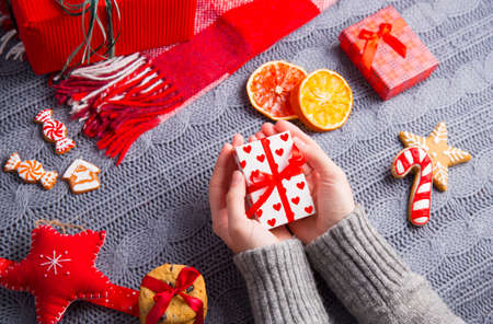 Female hands in gray knitted sweater holding romantic gift box with Christmas decor on background. New Year decoration with dried citrus fruits, cookies, gifts and gingerbread.の写真素材