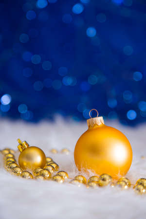 Golden Christmas balls and beads on white fur with garland lights on blue bokeh background.  New year card with empty space. Xmas festive decoration.の写真素材