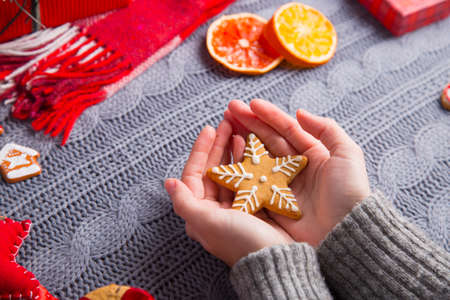 Female hands in gray knitted sweater holding gingerbread in form of star with Christmas decor on background. New Year decoration with dried citrus fruits, cookies, gifts and gingerbread.の写真素材