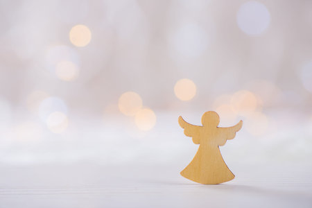 Wooden icon of Christmas angel on light bokeh background. Xmas card. Concept of love of religionの写真素材