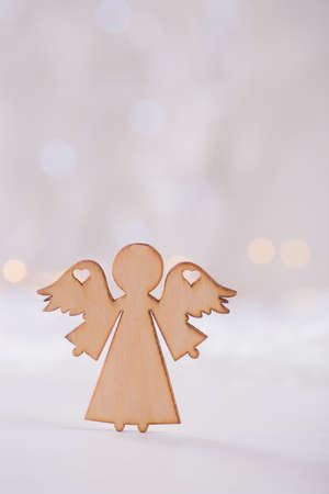 Wooden icon of Christmas angel with hole in form of heart on light bokeh background. Xmas card. Concept of love of religionの写真素材