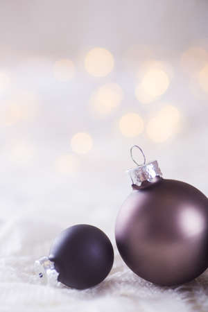 Two dark Christmas balls on white lace on light and warm bokeh background. New year card. Xmas decoration.の写真素材