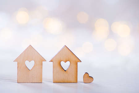 Two wooden houses with hole in the form of heart with little heart on light bokeh background. Romantic card. Concept of sweet home.の写真素材