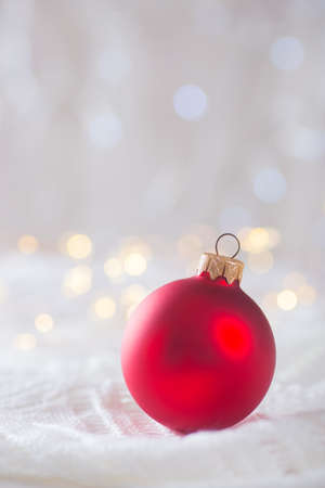 Red Christmas ball on white lace on light and warm bokeh background. New year card. Xmas decoration.の写真素材
