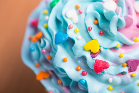 Closeup cupcake creamy multicolored top with colorful hearts and sprinkles on blue background....
