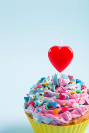Closeup festive creamy cupcake with sprinkles and candle in form of red heart on purple background. Romantic cake for Valentineâs dayの写真素材
