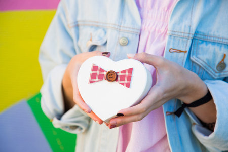 Female hands holding gift box in shape of heart in her hands on multicolored background. Romantic banner for Valentineâs day. の写真素材