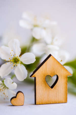 Wooden house with hole in form of heart surrounded by white flowering apricot branches on light background. Spring composition.の写真素材