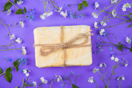 Wrapped paper gift box surrounded with blue and white little flowers on purple background. Spring present with flower frame.の写真素材