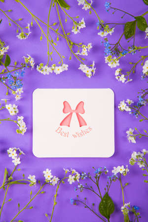 Greeting card with inscription "Best wishes" surrounded with blue and white little flowers on purple background. Spring card with flower frame.の写真素材
