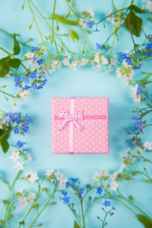 Pink gift box surrounded with blue and white little flowers on light mint background. Spring present with flower frame.の写真素材