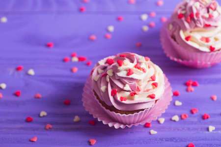 Two cupcakes with creamy pink and white top decorated with little hearts on purple wooden background. St. Valentine dessert.の写真素材