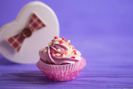 Cupcake with creamy pink and white top decorated with little hearts on purple background. St. Valentine dessert.の写真素材