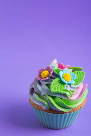Closeup cupcake creamy multicolored top decorated with colorful flowers and leaves on violet background. Spring cake for Motherâs dayの写真素材