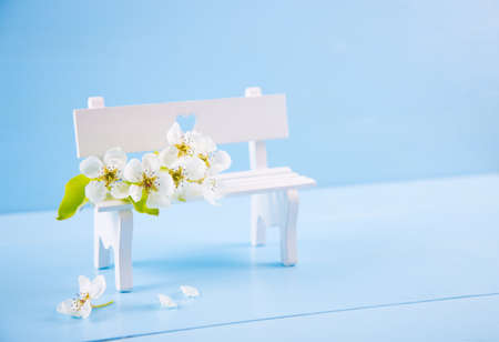 Beautiful tender flowering branch and white bench with hole in form of heart on blue wooden background. Spring romantic composition.の写真素材