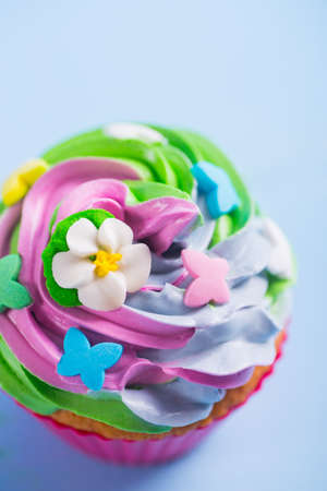 Closeup cupcake creamy multicolored top decorated with colorful flowers and butterflies on blue background. Spring cake for Motherâs dayの写真素材