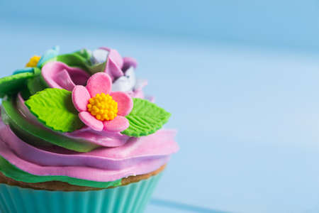 Closeup cupcake creamy multicolored top decorated with colorful flowers and leaves on blue background. Spring cake for Motherâs dayの写真素材