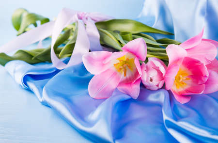 Beautiful bouquet of tender pink tulips lying on blue satin fabric. Spring card.の写真素材
