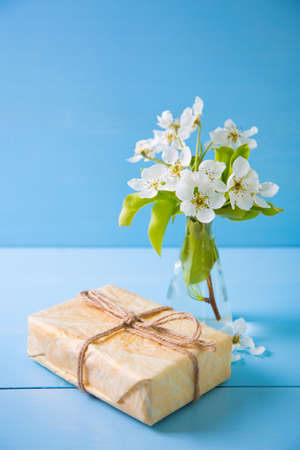 Gift box and bouquet of beautiful tender white flowering branches in glass vase on blue wooden background. Spring composition.の写真素材