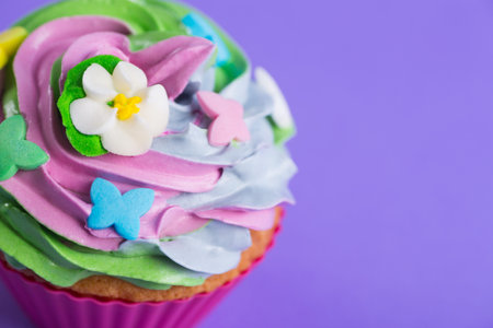 Closeup cupcake creamy multicolored top decorated with colorful flowers and butterflies on violet background. Spring cake for Motherâs dayの写真素材
