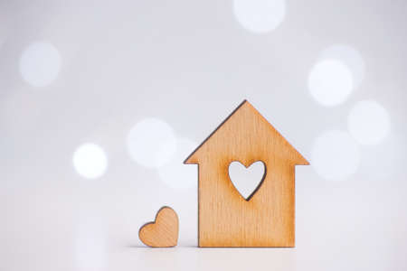 Wooden icon of house with hole in the form of heart with little heart on light bokeh background. Romantic card. Concept of sweet home.の写真素材