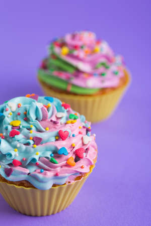 Two cupcakes with creamy multicolored top with colorful hearts and sprinkles on violet background. Romantic cake for Valentineâs dayの写真素材