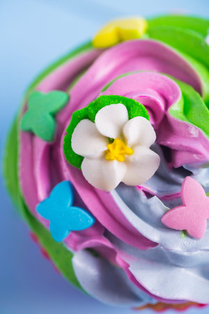 Closeup cupcake creamy multicolored top decorated with colorful flowers and butterflies on lilac background. Spring cake for Motherâs dayの写真素材