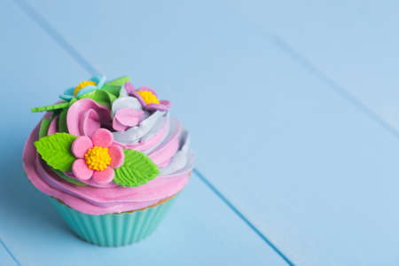 Closeup cupcake creamy multicolored top decorated with colorful flowers and leaves on blue wooden background. Spring cake for Motherâs dayの写真素材