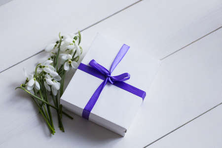Beautiful tender white snowdrops with gift box on white wooden background. Spring composition.の写真素材