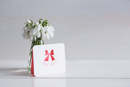 Bouquet of beautiful tender white snowdrops with greeting card on wooden background. Spring composition.の写真素材