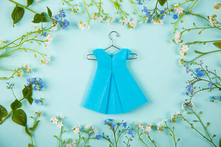 Blue paper origami dress on hanger surrounded with blue and white little flowers on light mint background. Tender Mothers Day card. Concept of spring fashion.の写真素材