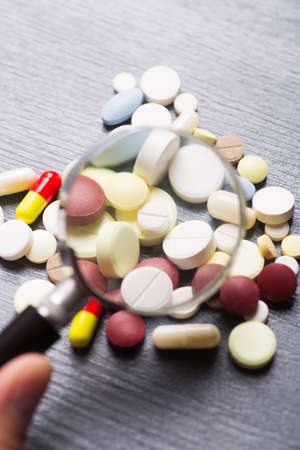 Colorful different capsules and pills under magnifying glass on gray background. Concept of medical research.の写真素材