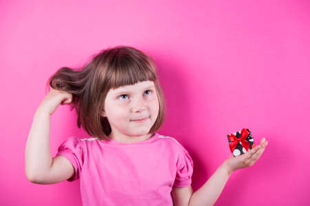 Funny little girl holding pretty spotted gift box in her hands on bright pink background. Mothers Day. Women's Day.の写真素材