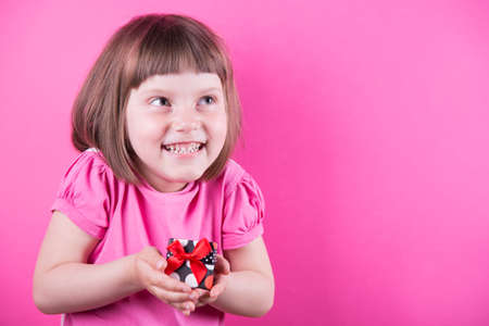 Happy smiling cute little girl holding pretty spotted gift box in her hands on bright pink background. Mothers Day. Women's Day.の写真素材