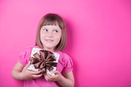 Funny smiling little girl holding pretty spotted gift box in her hands on bright pink background. Mothers Day. Women's Day.の写真素材