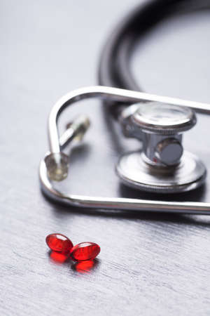 Closeup stethoscope near two red transparent capsules on gray table.の写真素材