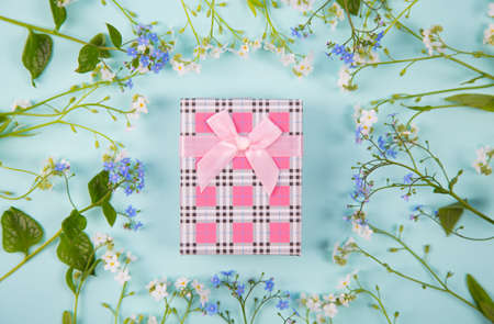Pink gift box surrounded with blue and white little flowers on light mint background. Spring present with flower frame.の写真素材