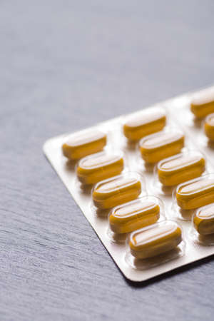 Yellow long pills in blister pack close-up on gray background.の写真素材