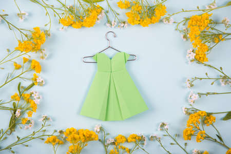 Green paper origami dress on hanger surrounded with yellow and white little flowers on light mint background. Tender Mothers Day card. Concept of spring fashion.の写真素材