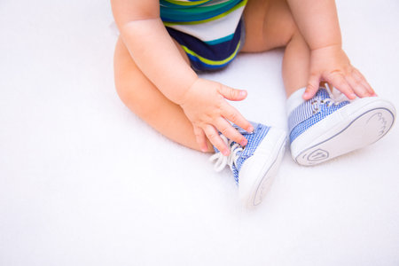 Legs of baby boy dressed in children's blue sneakers on lacing on white background. Concept of first...
