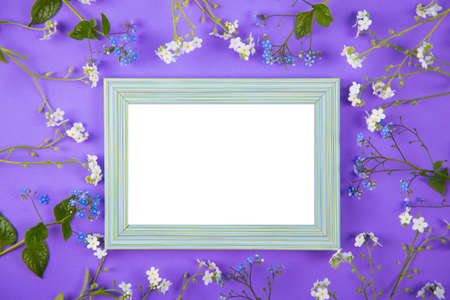 Empty photo frame surrounded with blue and white little flowers on violet background. Spring card with clear space.の写真素材