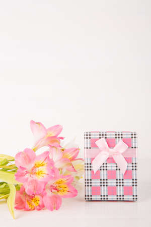 Pink gift box with tender bouquet of beautiful alstroemeria flowers on white wooden background. Spring card for women's or mother's day with empty space.の写真素材