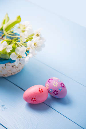 Two painted pink Easter eggs near basket with white spring flowering branch on light blue background.の写真素材