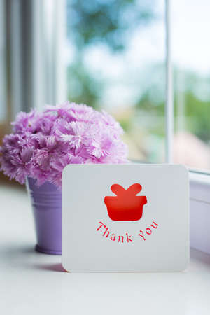 Little purple bucket with tender bouquet of beautiful pink carnation and greeting card with inscription "Thank you" near window in daylight. Spring motherâs day gift.の写真素材