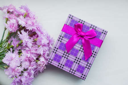 Bouquet of tender pink carnation flowers with purple gift box on light background in daylight. Spring Motherâs day gift.の写真素材