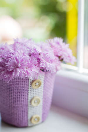 Purple basket with tender bouquet of beautiful pink carnation near window in daylight. Spring motherâs day card.の写真素材