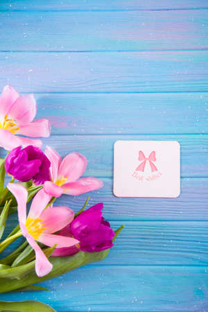 Greeting card with inscription "Best wishes" and tender bouquet of beautiful pink tulips on creative blue wooden background. Concept of spring gift.の写真素材