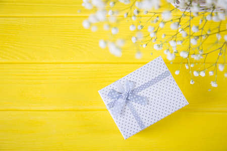 Gift box and fresh bouquet of white gypsophila on yellow wooden background. Concept of Mother's day gift.の写真素材