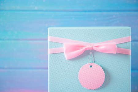 Closeup cute mint blue gift box with pink bow and label for signature and greetings on blue wooden background.の写真素材